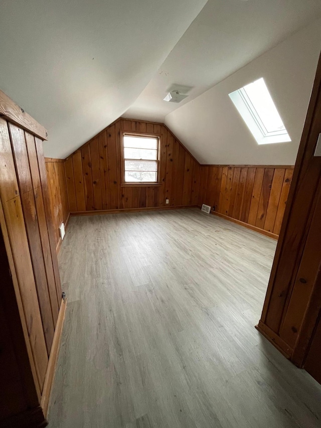 bonus room featuring wooden walls, lofted ceiling with skylight, and light hardwood / wood-style flooring