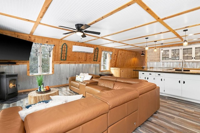 living room with sink, a wood stove, hardwood / wood-style flooring, ceiling fan, and a wall unit AC