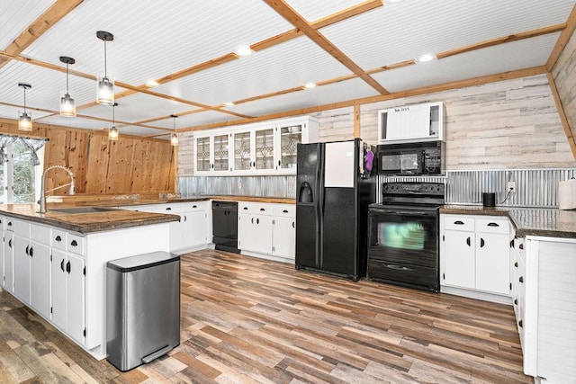 kitchen with white cabinets, wooden walls, sink, and black appliances