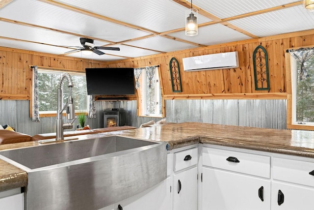 kitchen with pendant lighting, wooden walls, sink, white cabinets, and a wall unit AC