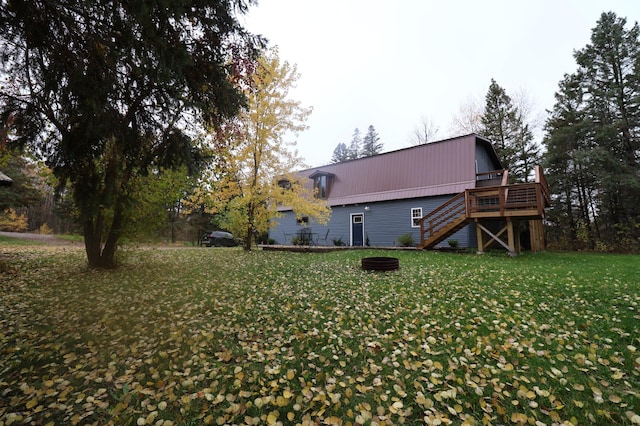 back of property featuring an outdoor fire pit, a deck, and a lawn