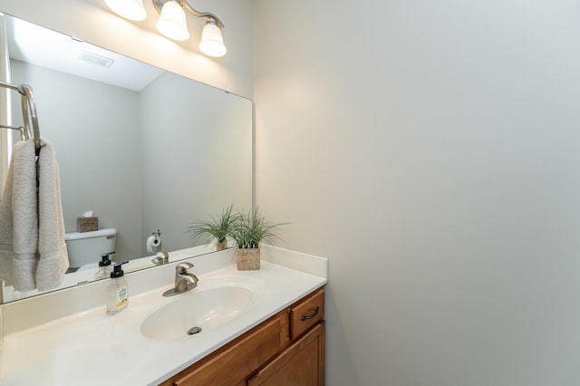 bathroom with toilet, vanity, and visible vents