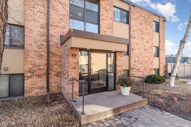 doorway to property featuring a patio area, brick siding, fence, and stucco siding