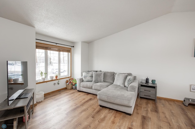 living area featuring light wood-type flooring, baseboards, vaulted ceiling, and a textured ceiling