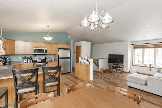 kitchen featuring appliances with stainless steel finishes, open floor plan, a peninsula, vaulted ceiling, and light wood-style floors