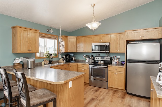 kitchen with a peninsula, light brown cabinets, appliances with stainless steel finishes, and a sink