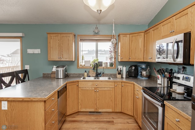 kitchen featuring lofted ceiling, a textured ceiling, a peninsula, a sink, and appliances with stainless steel finishes