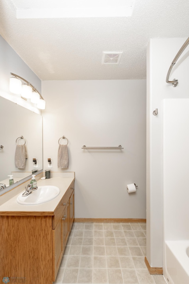 full bathroom with a textured ceiling, a bathing tub, vanity, visible vents, and baseboards