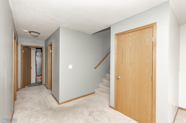 hall featuring baseboards, stairway, a textured ceiling, and light colored carpet