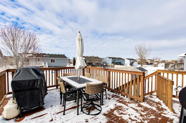 snow covered deck featuring outdoor dining space, a grill, and a residential view