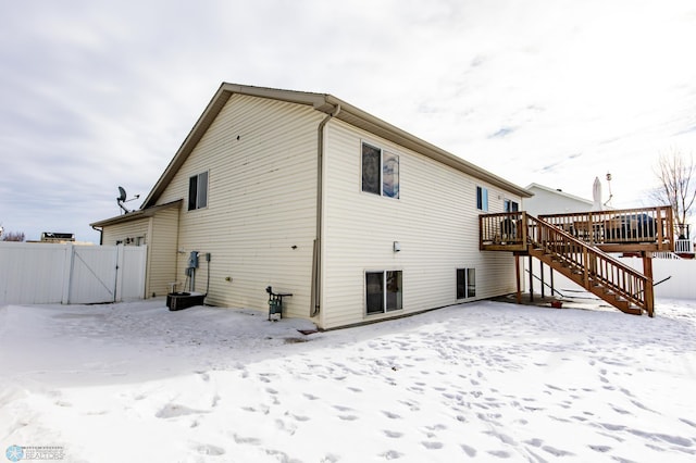 snow covered back of property with a deck, stairway, fence, and a gate