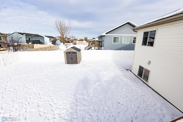 snowy yard featuring a shed, an outdoor structure, fence, and a residential view