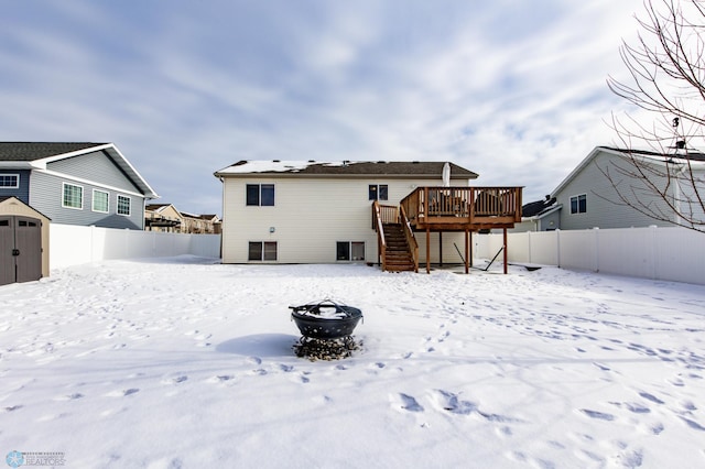 snow covered back of property with a deck, a storage unit, an outdoor fire pit, and a fenced backyard