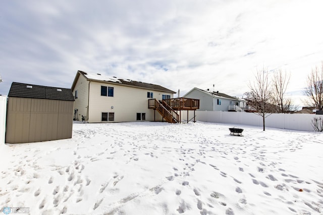 snow covered house with stairway, a storage shed, fence, a deck, and an outdoor structure