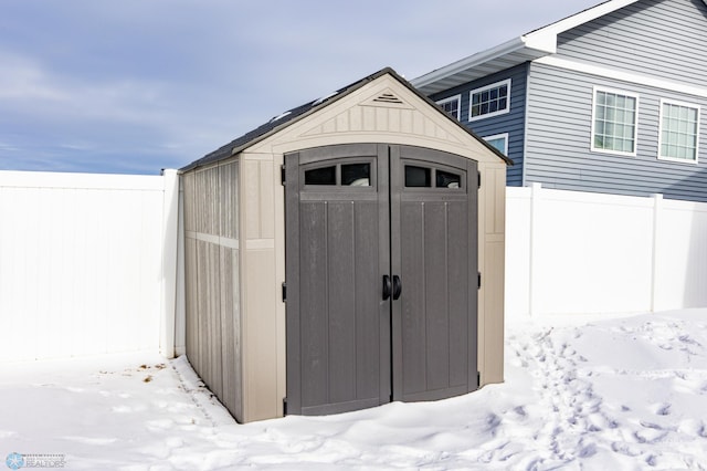 snow covered structure featuring a storage shed, fence, and an outbuilding