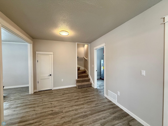 spare room featuring dark wood-type flooring, water heater, and a textured ceiling