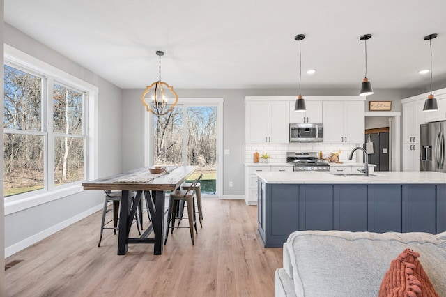 kitchen featuring sink, backsplash, stainless steel appliances, white cabinets, and decorative light fixtures