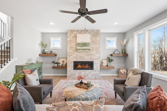 living room with a fireplace, ceiling fan, and light wood-type flooring