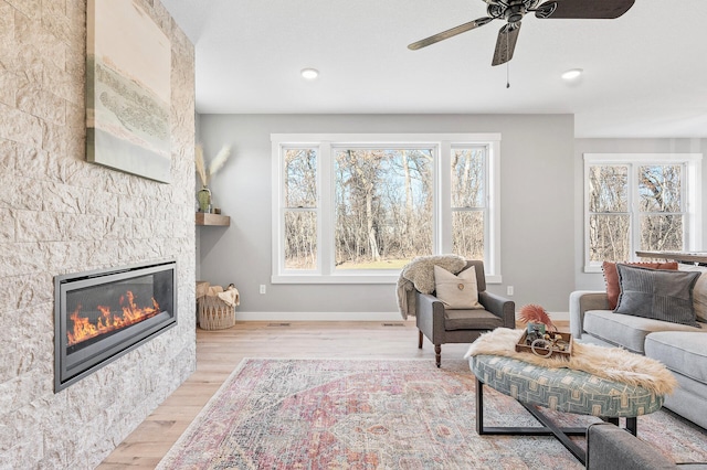 living room featuring a stone fireplace, light hardwood / wood-style floors, and ceiling fan