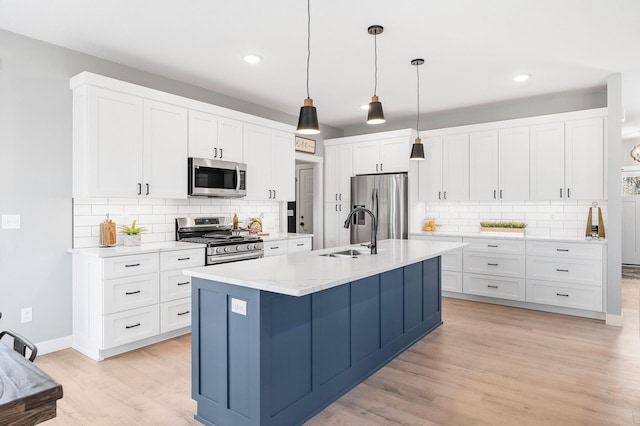 kitchen with sink, appliances with stainless steel finishes, white cabinetry, hanging light fixtures, and a center island with sink