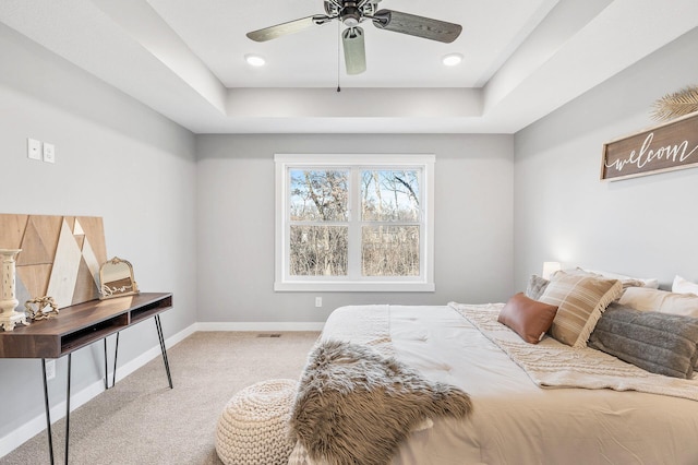 bedroom featuring ceiling fan, a tray ceiling, and light carpet