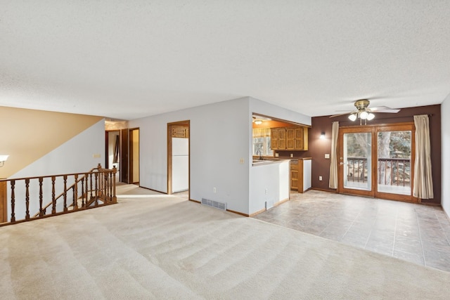 unfurnished living room featuring ceiling fan with notable chandelier, sink, light carpet, and a textured ceiling