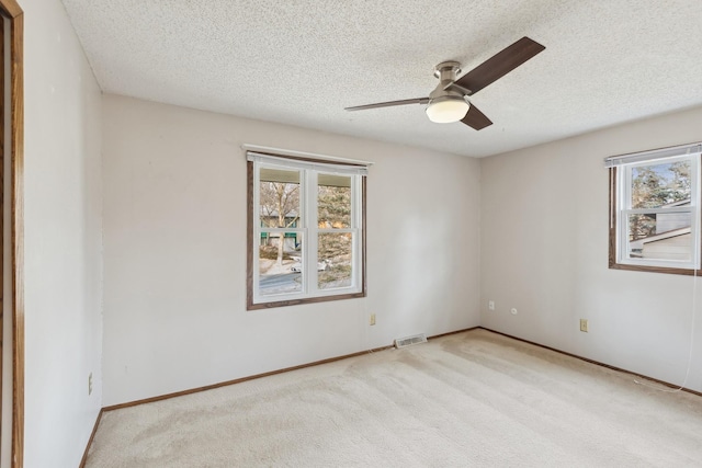 carpeted empty room with ceiling fan, a healthy amount of sunlight, and a textured ceiling