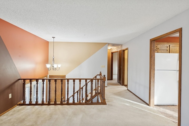 corridor with a textured ceiling, light colored carpet, and a chandelier