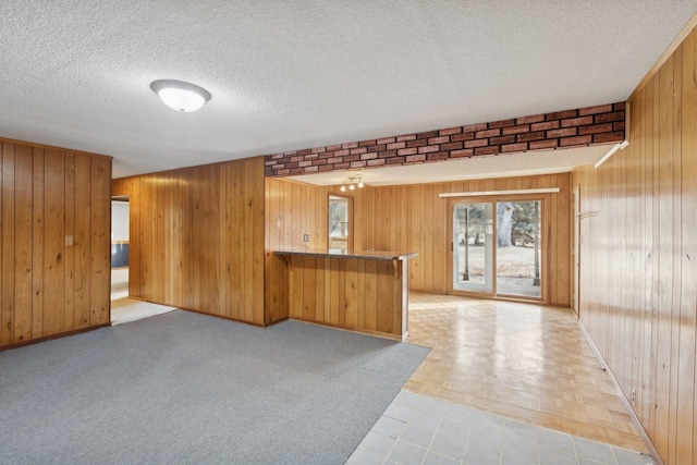 kitchen with wooden walls, kitchen peninsula, a textured ceiling, and a kitchen bar