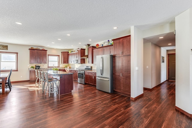 kitchen featuring a kitchen breakfast bar, a kitchen island, dark wood finished floors, stainless steel appliances, and baseboards