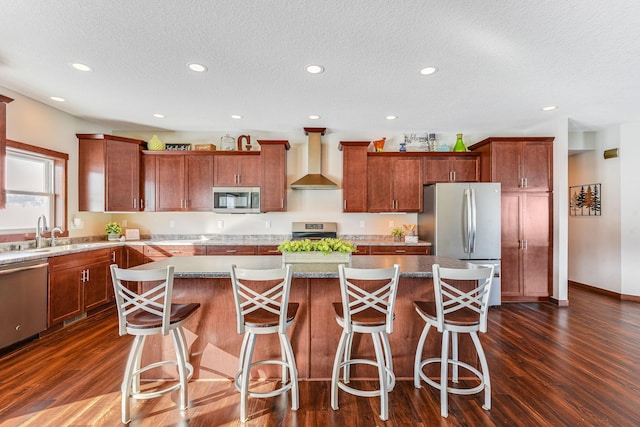 kitchen featuring dark wood finished floors, a sink, stainless steel appliances, wall chimney exhaust hood, and a center island