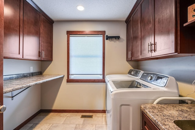 clothes washing area featuring a textured ceiling, cabinet space, baseboards, and washer and clothes dryer