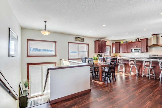 kitchen featuring a breakfast bar area, light countertops, appliances with stainless steel finishes, wall chimney exhaust hood, and dark wood-style flooring