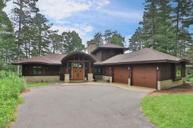 prairie-style house featuring aphalt driveway, roof with shingles, a chimney, stone siding, and an attached garage