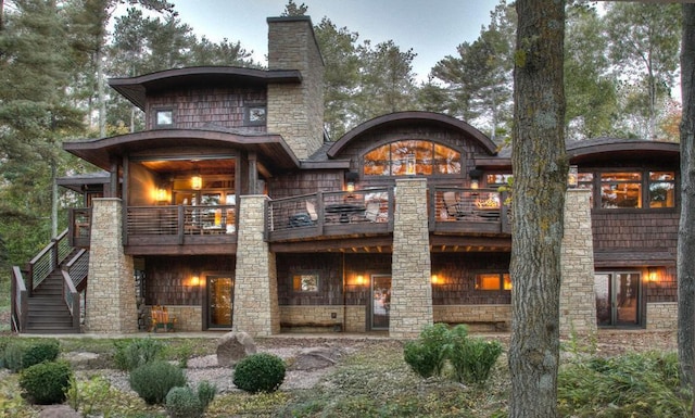 rear view of house featuring stone siding, a chimney, and a balcony