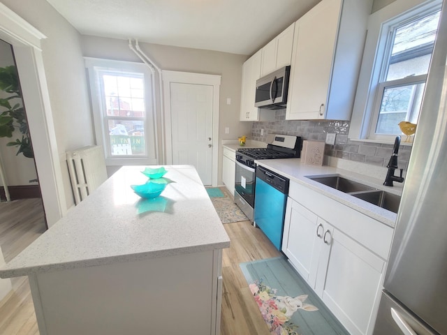 kitchen with sink, appliances with stainless steel finishes, white cabinetry, backsplash, and a center island