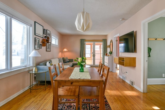 dining space with french doors, a textured ceiling, light hardwood / wood-style flooring, and a wealth of natural light