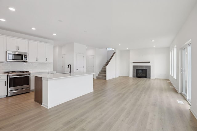 kitchen with appliances with stainless steel finishes, white cabinetry, backsplash, a kitchen island with sink, and a tiled fireplace