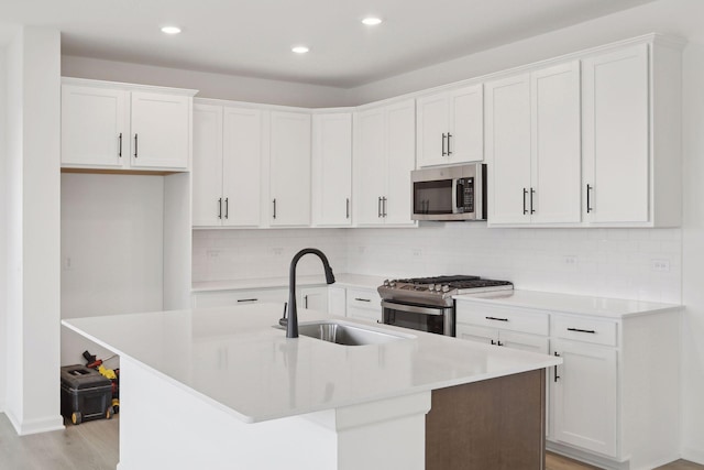 kitchen with stainless steel appliances, white cabinetry, sink, and a center island with sink