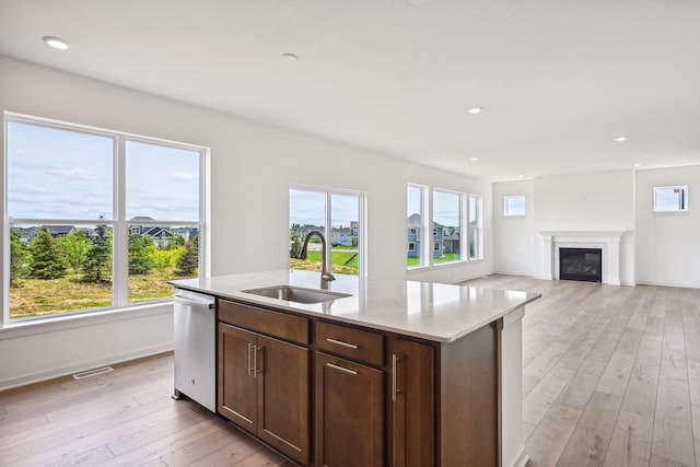 kitchen with sink, a kitchen island with sink, a wealth of natural light, stainless steel dishwasher, and light wood-type flooring