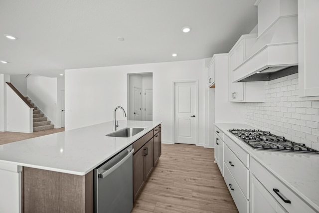 kitchen featuring a sink, white cabinetry, appliances with stainless steel finishes, custom exhaust hood, and a center island with sink