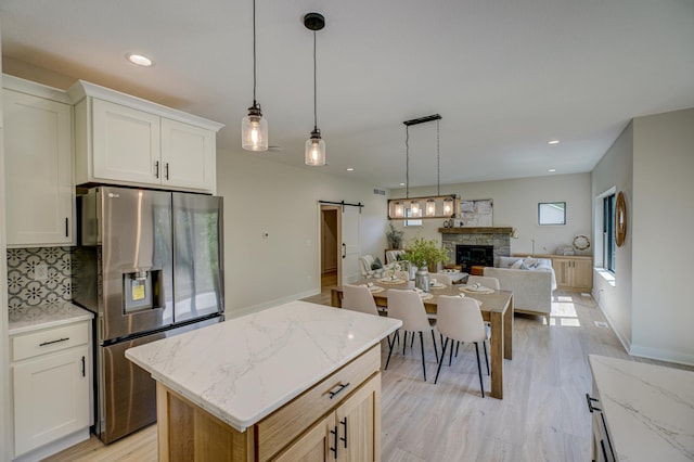 1205 Riverside Dr N, North Hudson, WI 54016 - kitchen featuring stainless steel fridge with ice dispenser, a barn door, a stone fireplace, open floor plan, and tasteful backsplash