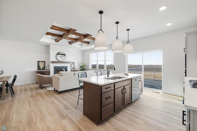 kitchen featuring light countertops, light wood-style floors, coffered ceiling, stainless steel dishwasher, and a sink