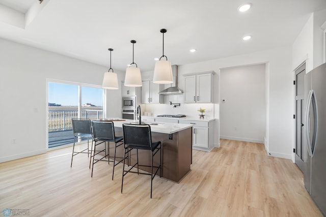 kitchen featuring light wood-type flooring, light countertops, wall chimney exhaust hood, appliances with stainless steel finishes, and a sink
