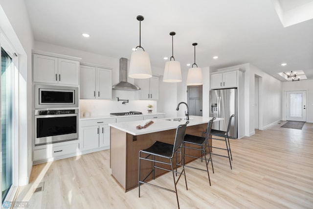 kitchen with a sink, wall chimney range hood, light countertops, light wood finished floors, and stainless steel appliances