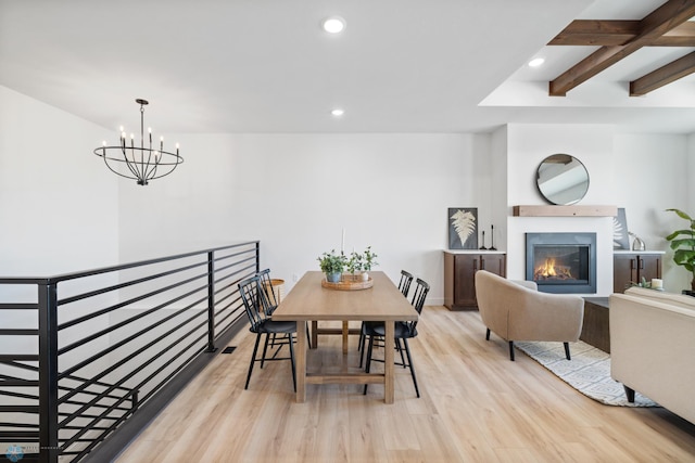 dining area featuring an inviting chandelier, beam ceiling, recessed lighting, light wood-style flooring, and a glass covered fireplace