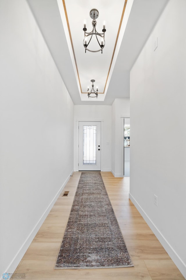 foyer with light wood finished floors, a notable chandelier, visible vents, and a raised ceiling