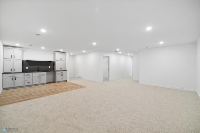finished basement with visible vents, baseboards, indoor wet bar, recessed lighting, and light colored carpet