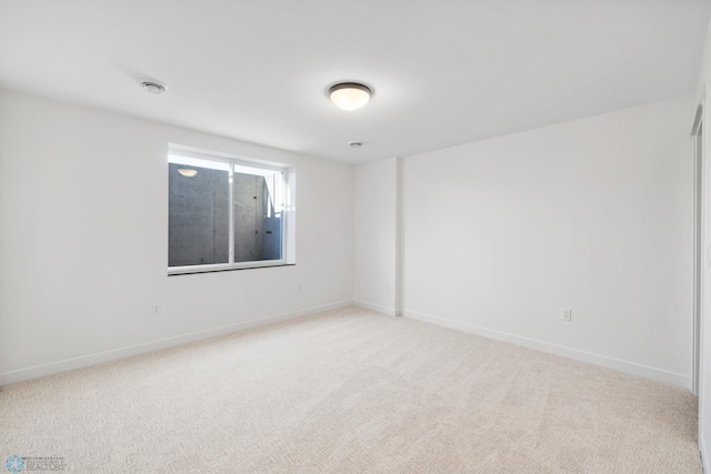 spare room featuring light colored carpet and baseboards