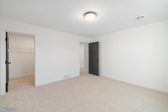 unfurnished bedroom featuring a walk in closet, light carpet, baseboards, and visible vents
